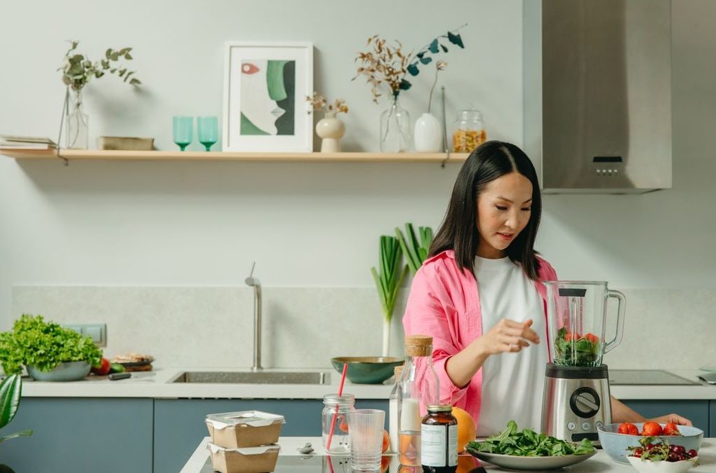 Asian woman blending fresh fruits and vegetables in a stylish kitchen setting.