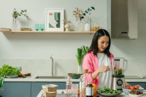 Asian woman blending fresh fruits and vegetables in a stylish kitchen setting.