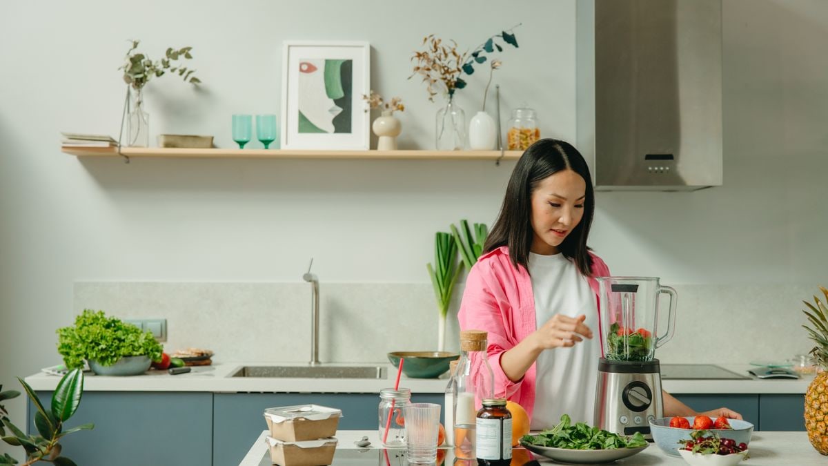 Asian woman blending fresh fruits and vegetables in a stylish kitchen setting.